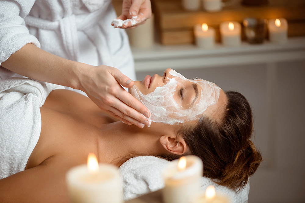 Young beautiful brunette girl in mask for face relaxing in spa salon. Eyes closed. Copy space.